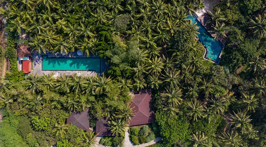 Top-down aerial view of multiple swimming pools set within dense tropical greenery at a peaceful beachside resort in North Goa!